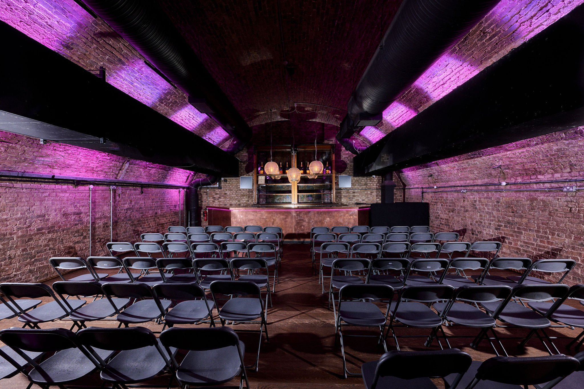 Versatile industrial event space with exposed brick and purple lighting for workshops.