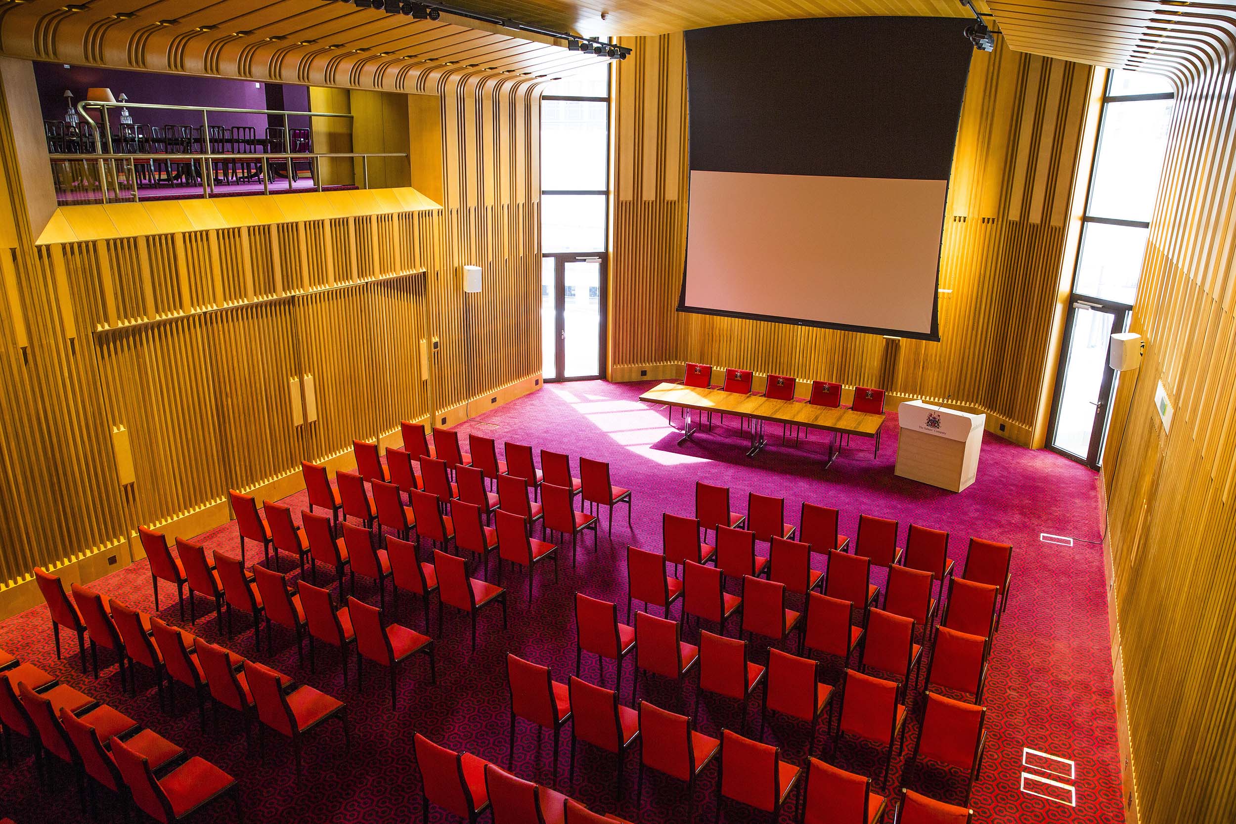 Modern meeting space in Salters' Hall with wooden paneling and vibrant red chairs.