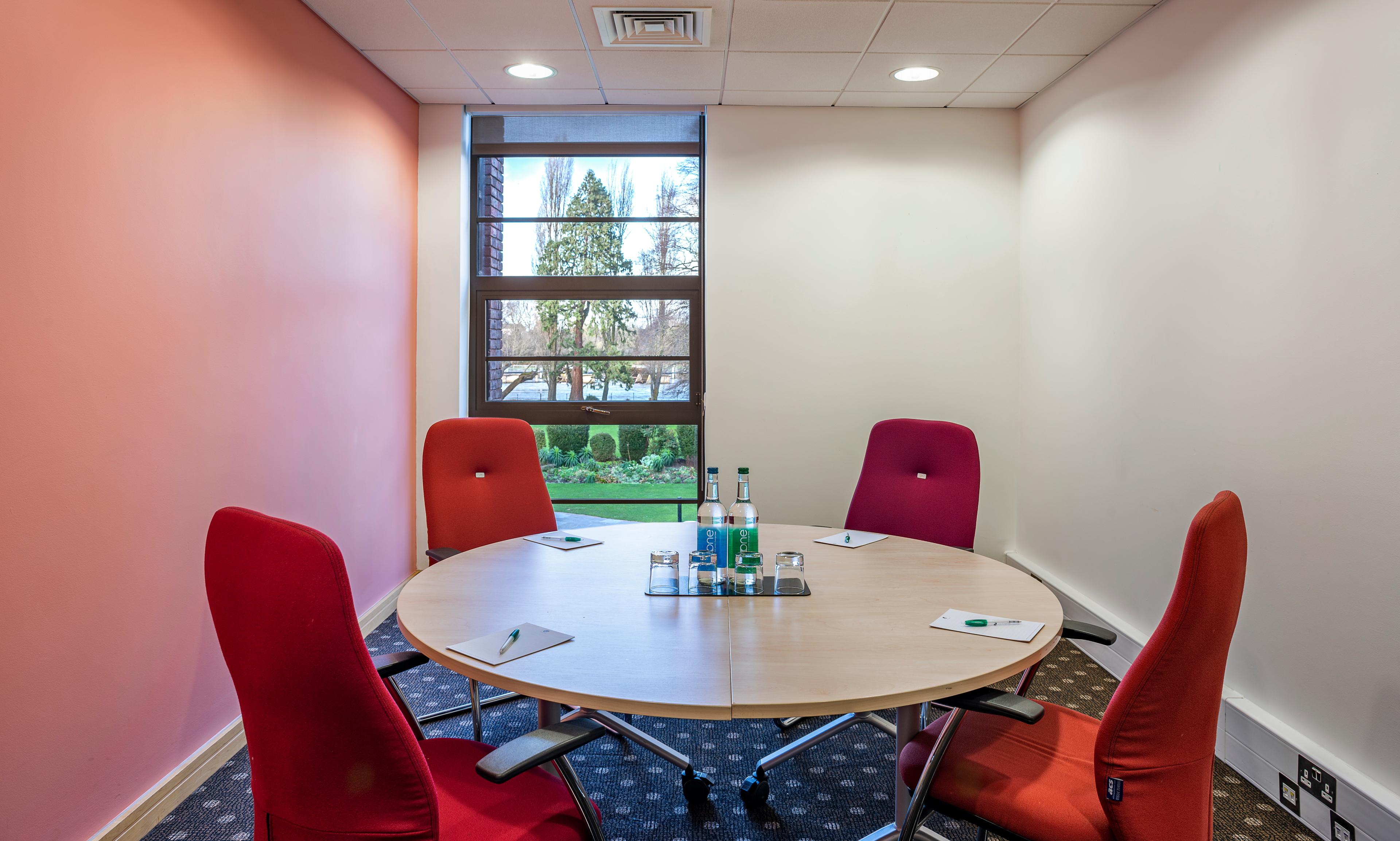 Modern meeting room with round table and red chairs at The Lensbury for collaborative events.