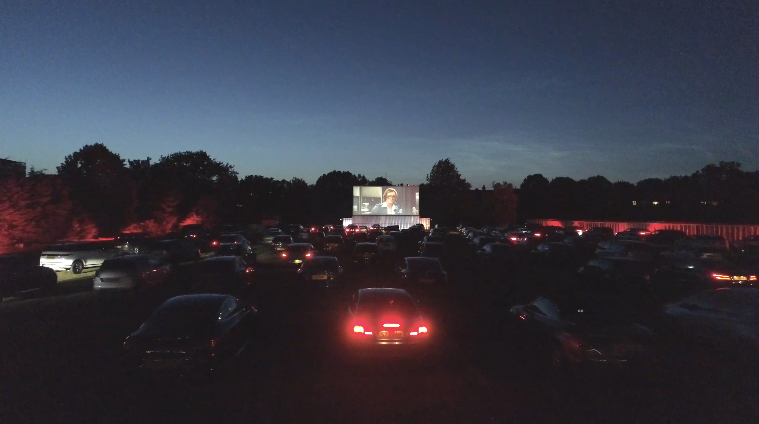 Vibrant outdoor movie event at Sunset Cinema with cars and large screen. - Banner