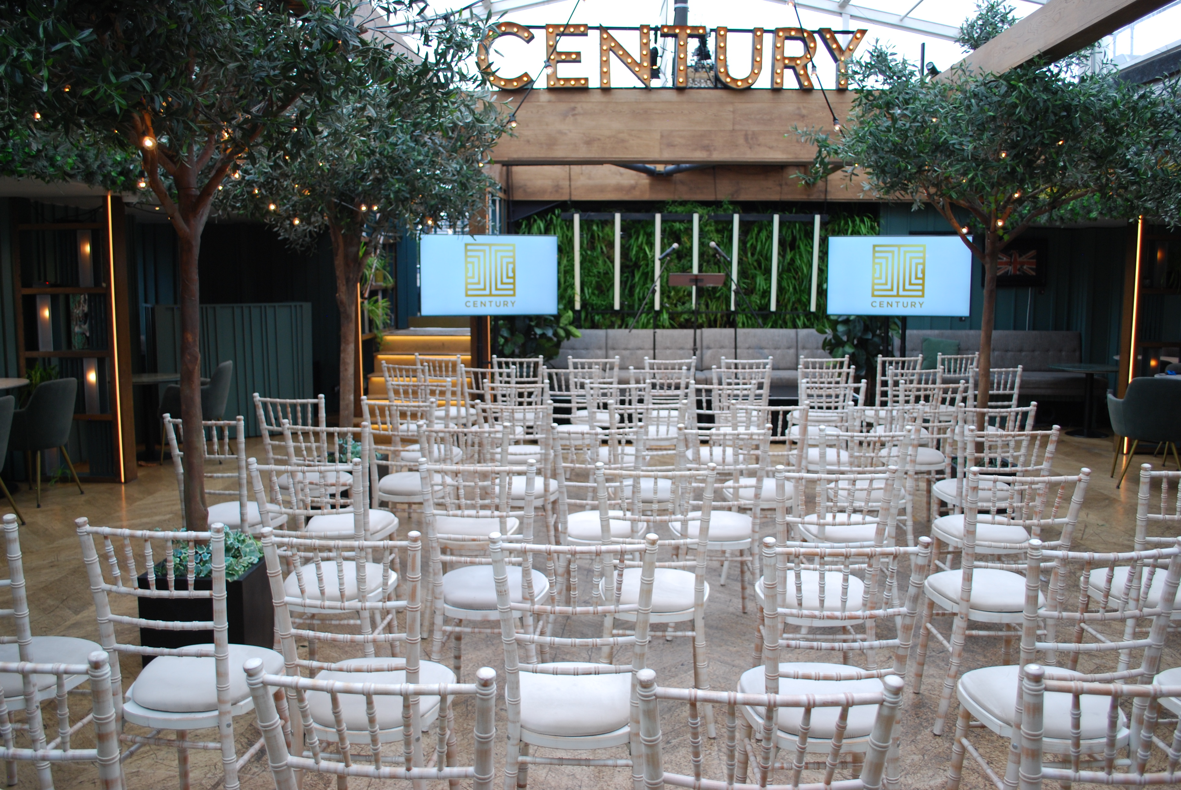 Roof terrace conference with retractable glass roof, elegant chairs, and dual screens.