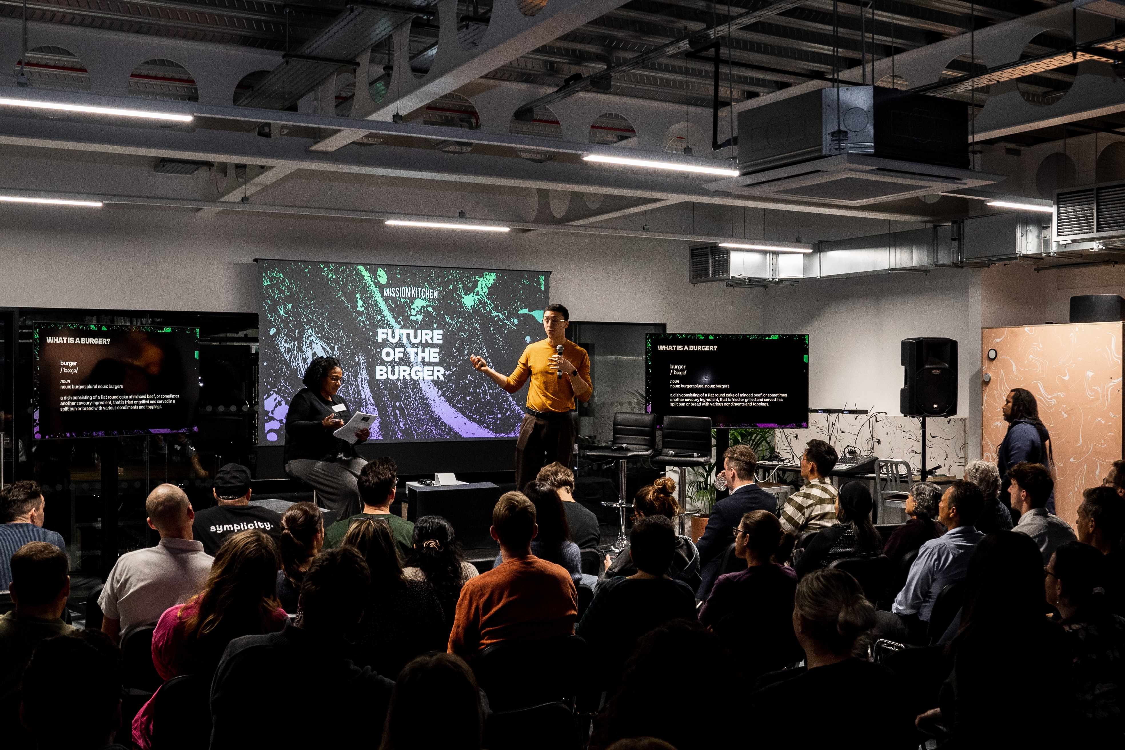 Engaging speaker in modern Glass Room event space for workshops and panel discussions. - Banner