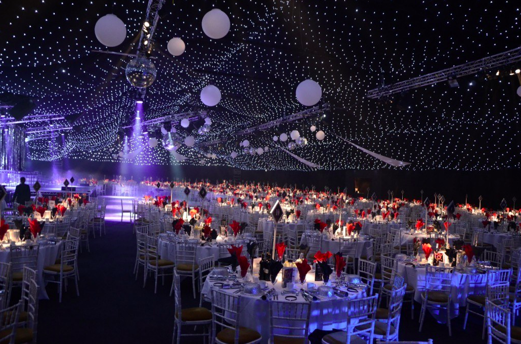 Aintree Racecourse gala with elegant tables and red floral centerpieces under starry canopy. - Banner